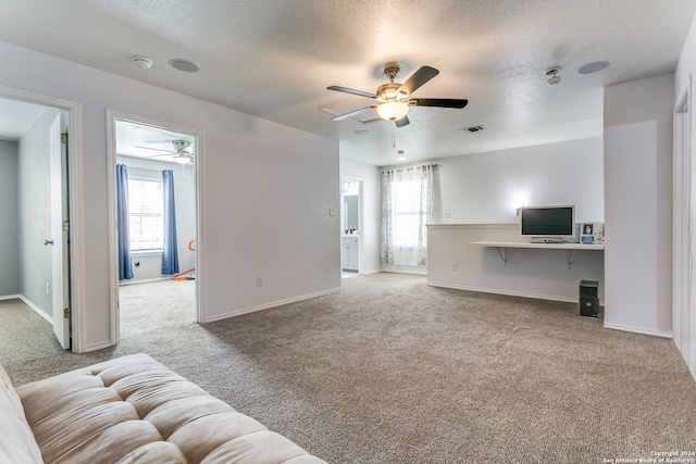 carpeted living room with built in desk, ceiling fan, and a textured ceiling