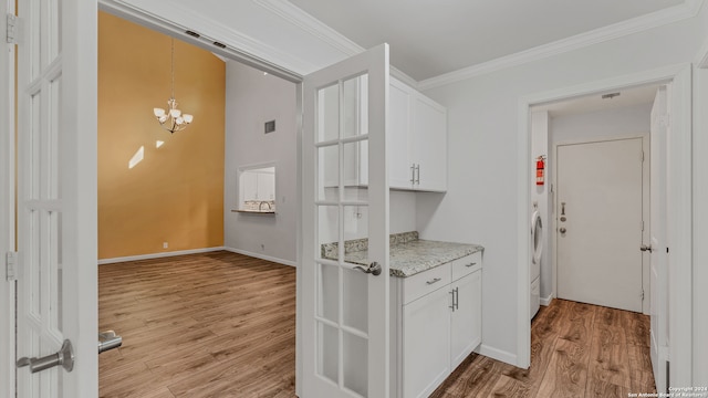 kitchen with crown molding, white cabinets, a notable chandelier, and light hardwood / wood-style floors