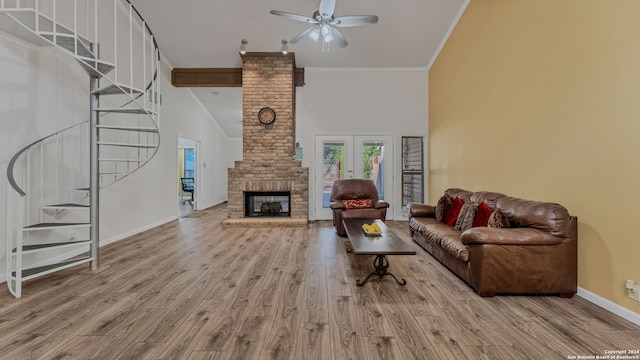 living room with ceiling fan, a brick fireplace, ornamental molding, a high ceiling, and light hardwood / wood-style floors