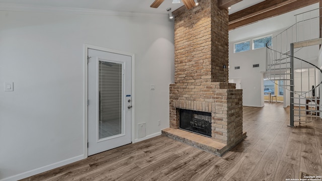 unfurnished living room with a high ceiling, beamed ceiling, wood-type flooring, ornamental molding, and a brick fireplace