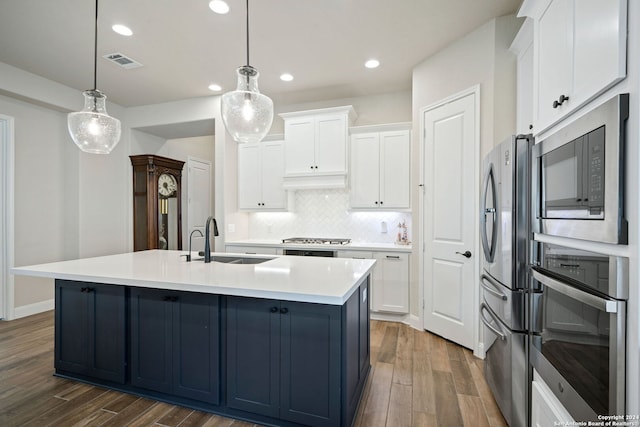 kitchen with white cabinetry, sink, stainless steel appliances, decorative light fixtures, and a center island with sink