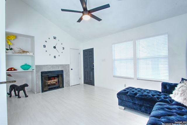 living room with ceiling fan, high vaulted ceiling, wood-type flooring, a tile fireplace, and built in shelves