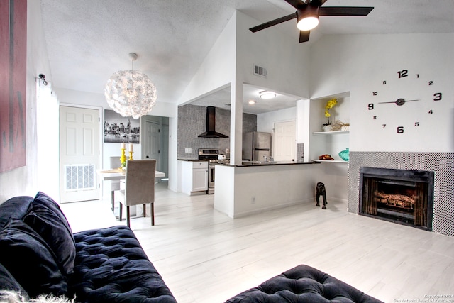 living room featuring a textured ceiling, a tiled fireplace, high vaulted ceiling, and ceiling fan with notable chandelier