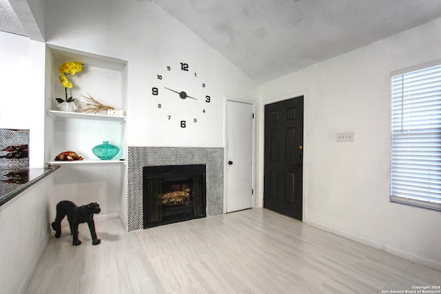 living room with a tiled fireplace, light hardwood / wood-style flooring, a textured ceiling, and lofted ceiling