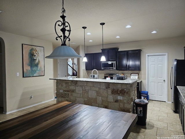 kitchen with an island with sink, light stone countertops, sink, pendant lighting, and stainless steel appliances