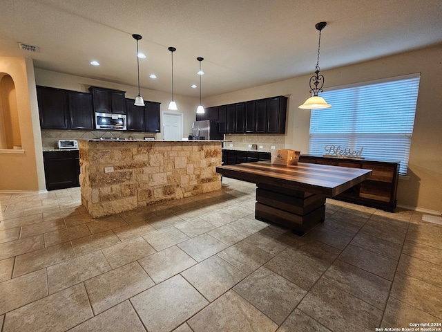 kitchen with appliances with stainless steel finishes, decorative backsplash, decorative light fixtures, and a kitchen island