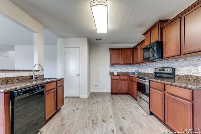 kitchen featuring light hardwood / wood-style flooring, dark stone countertops, sink, black appliances, and a textured ceiling