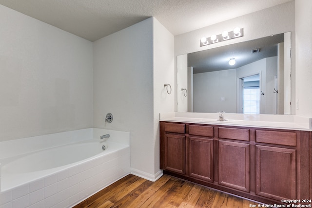 bathroom with vanity, a textured ceiling, hardwood / wood-style flooring, and tiled bath