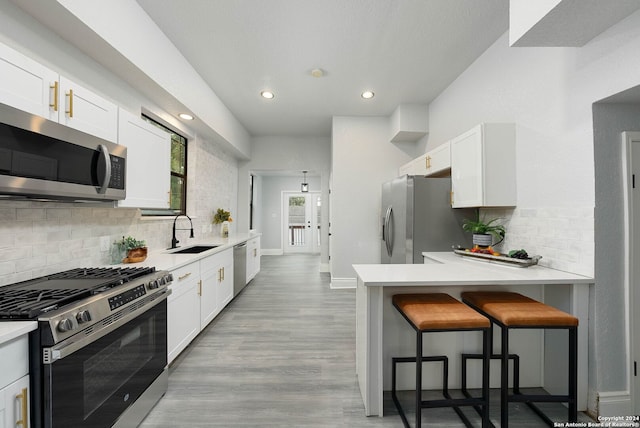 kitchen with a breakfast bar area, light hardwood / wood-style flooring, stainless steel appliances, sink, and white cabinets