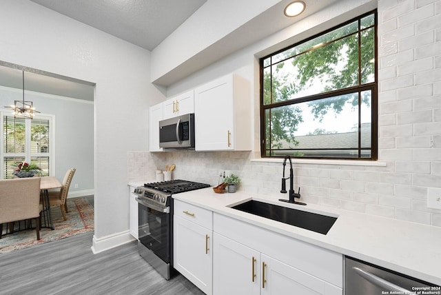 kitchen with backsplash, sink, white cabinets, appliances with stainless steel finishes, and light hardwood / wood-style floors