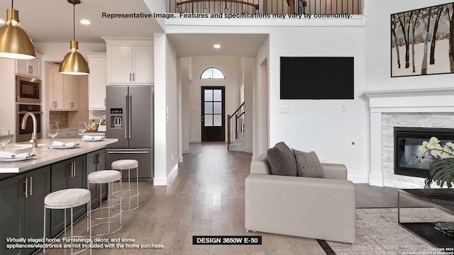 kitchen featuring a towering ceiling, appliances with stainless steel finishes, hanging light fixtures, white cabinetry, and hardwood / wood-style flooring