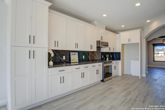 kitchen with white cabinets, backsplash, stainless steel appliances, and light hardwood / wood-style flooring