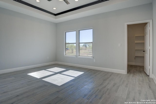 empty room with a tray ceiling, crown molding, and light hardwood / wood-style floors