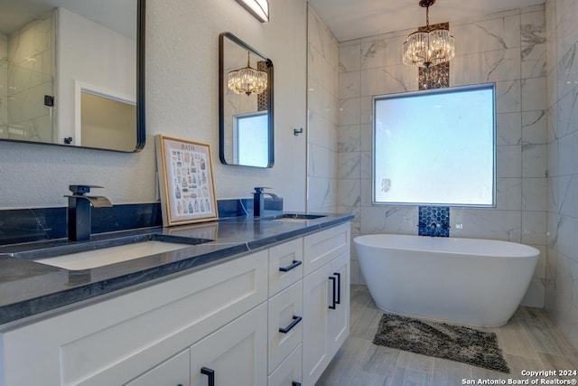 bathroom with vanity, an inviting chandelier, a washtub, tile walls, and wood-type flooring