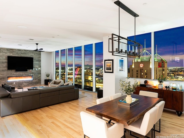 dining area featuring a fireplace, ceiling fan with notable chandelier, light wood-type flooring, and floor to ceiling windows