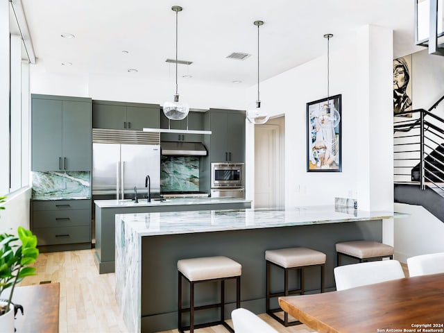 kitchen featuring built in appliances, a breakfast bar, tasteful backsplash, and light hardwood / wood-style flooring