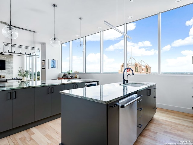 kitchen with gray cabinetry, sink, decorative light fixtures, light hardwood / wood-style flooring, and a center island with sink