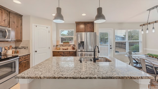 kitchen with appliances with stainless steel finishes, a kitchen island with sink, sink, and hanging light fixtures