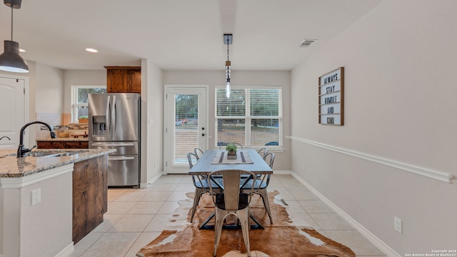 kitchen featuring stone countertops, hanging light fixtures, sink, stainless steel fridge, and light tile patterned floors