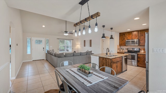 kitchen with an island with sink, stainless steel appliances, sink, pendant lighting, and light stone counters