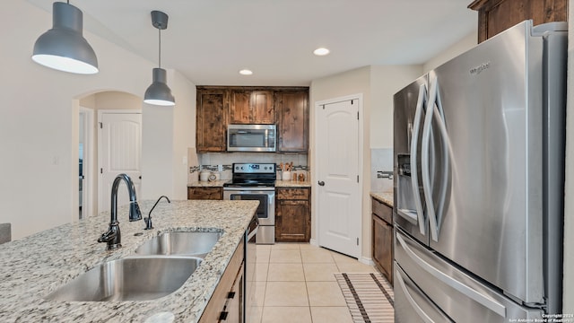 kitchen with light stone countertops, sink, light tile patterned flooring, stainless steel appliances, and decorative light fixtures