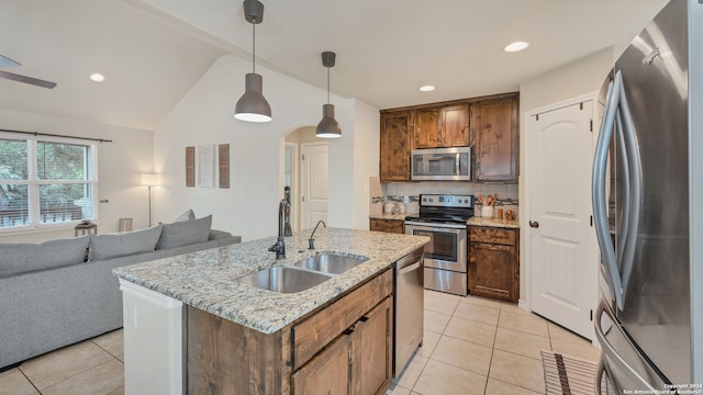 kitchen featuring lofted ceiling, stainless steel appliances, sink, light stone countertops, and decorative light fixtures