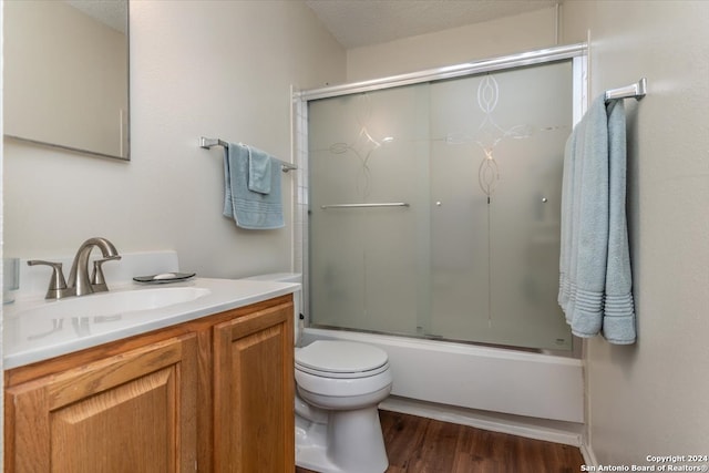 full bathroom with hardwood / wood-style floors, bath / shower combo with glass door, a textured ceiling, toilet, and vanity