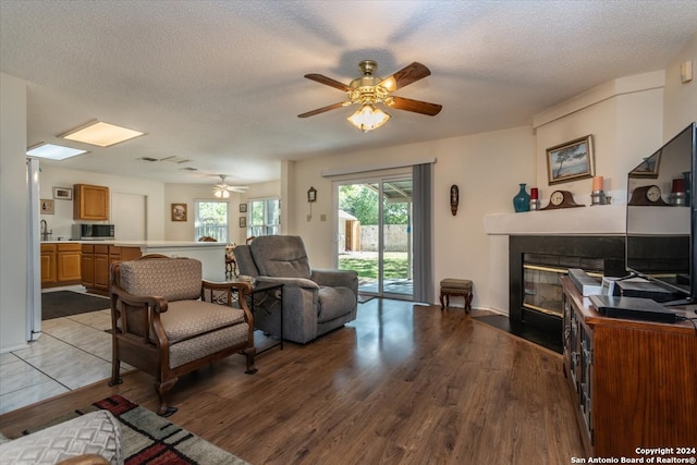 living room with light hardwood / wood-style floors, a textured ceiling, and ceiling fan