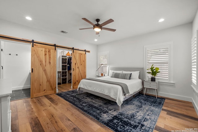 bedroom featuring wood-type flooring, a barn door, ceiling fan, a closet, and a walk in closet