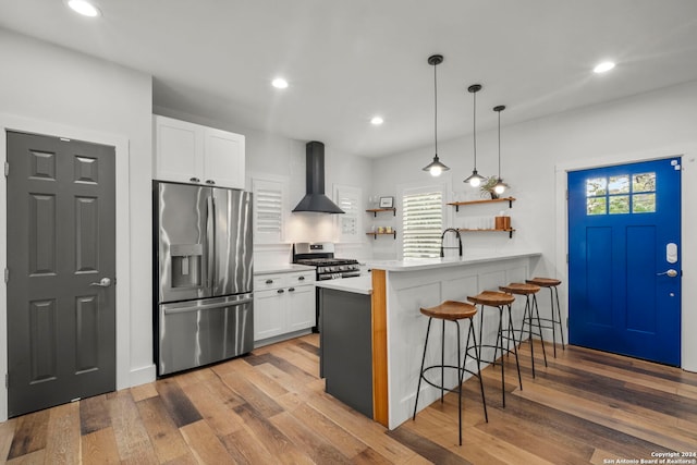 kitchen with white cabinetry, appliances with stainless steel finishes, wall chimney range hood, a kitchen breakfast bar, and kitchen peninsula