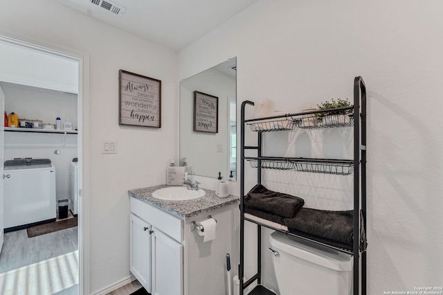 bathroom with vanity, toilet, wood-type flooring, and washing machine and clothes dryer