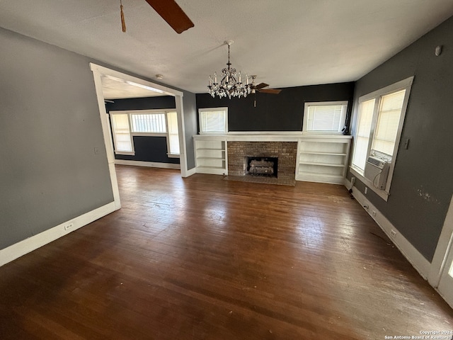 unfurnished living room featuring dark wood-type flooring, cooling unit, a brick fireplace, and ceiling fan with notable chandelier