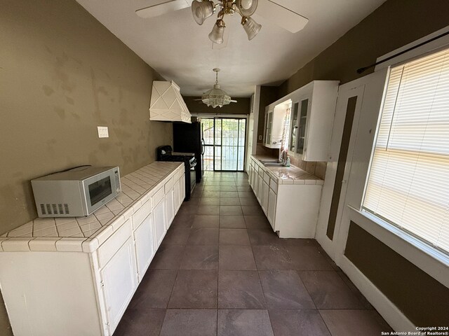 kitchen featuring black electric range oven, tile counters, hanging light fixtures, sink, and white cabinets