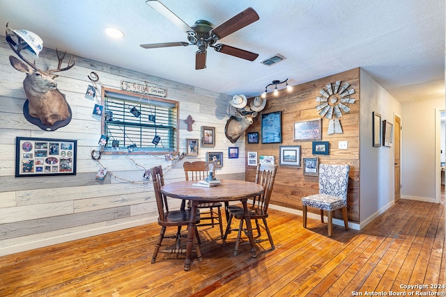 dining space featuring ceiling fan, hardwood / wood-style flooring, a textured ceiling, and wooden walls