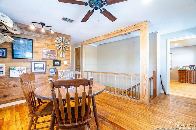 dining room with wooden walls, light wood-type flooring, and ceiling fan