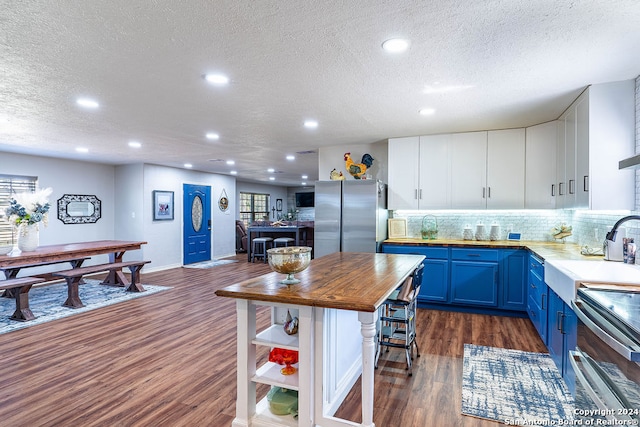 kitchen featuring appliances with stainless steel finishes, a textured ceiling, blue cabinets, white cabinetry, and dark hardwood / wood-style floors