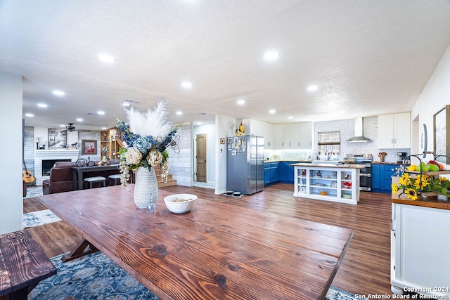 dining room featuring a large fireplace, sink, dark hardwood / wood-style flooring, a textured ceiling, and ceiling fan