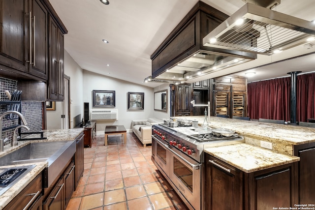 kitchen featuring tasteful backsplash, light stone countertops, appliances with stainless steel finishes, dark brown cabinets, and lofted ceiling