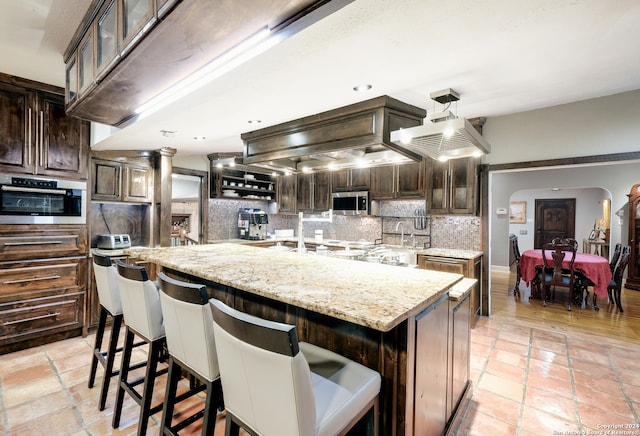 kitchen featuring tasteful backsplash, a spacious island, a breakfast bar, light stone countertops, and stainless steel appliances