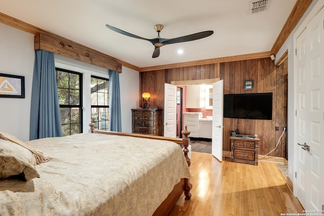 bedroom with ceiling fan, connected bathroom, wood-type flooring, ornamental molding, and wooden walls