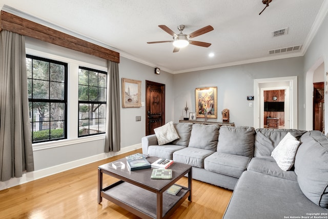 living room featuring light hardwood / wood-style floors, a textured ceiling, ornamental molding, and ceiling fan