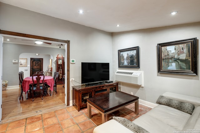 living room with a wall mounted AC, light wood-type flooring, and ceiling fan