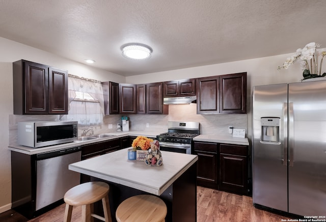 kitchen with appliances with stainless steel finishes, a center island, hardwood / wood-style floors, dark brown cabinetry, and a breakfast bar area