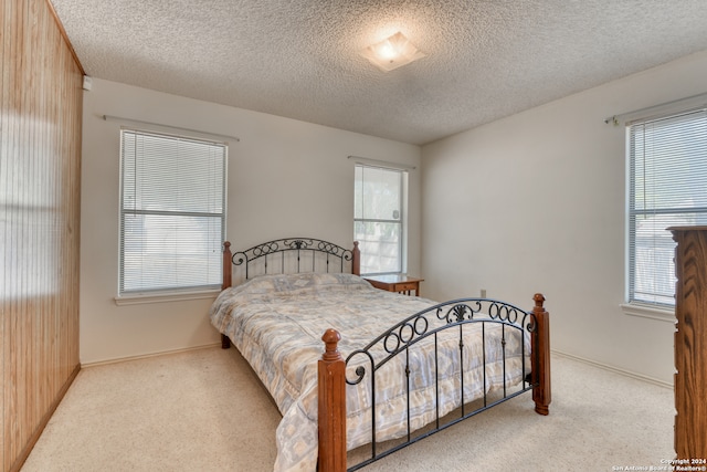 carpeted bedroom with multiple windows, wood walls, and a textured ceiling