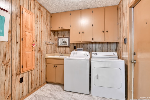 laundry room with wooden walls, independent washer and dryer, sink, cabinets, and a textured ceiling