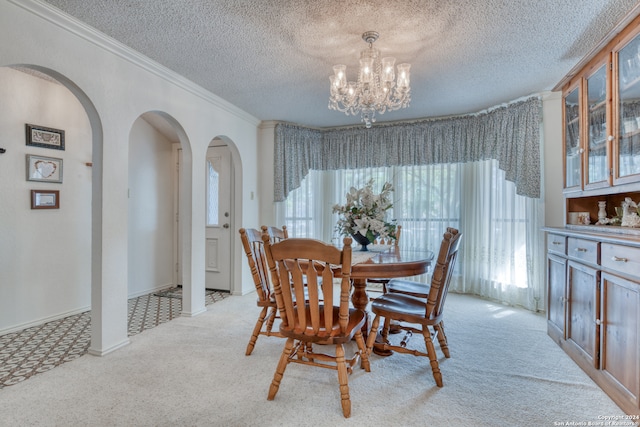 dining room featuring light carpet, a notable chandelier, ornamental molding, and a textured ceiling