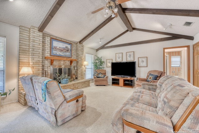 carpeted living room with a textured ceiling, lofted ceiling with beams, ceiling fan, and a brick fireplace