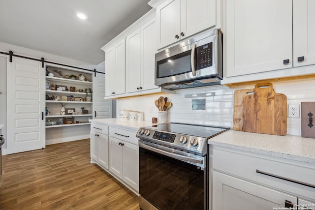 kitchen featuring wood-type flooring, stainless steel appliances, a barn door, white cabinets, and light stone counters