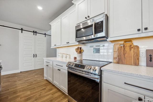 kitchen with a barn door, light hardwood / wood-style flooring, stainless steel appliances, and white cabinets