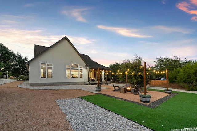 back house at dusk featuring an outdoor fire pit, a patio area, and a lawn